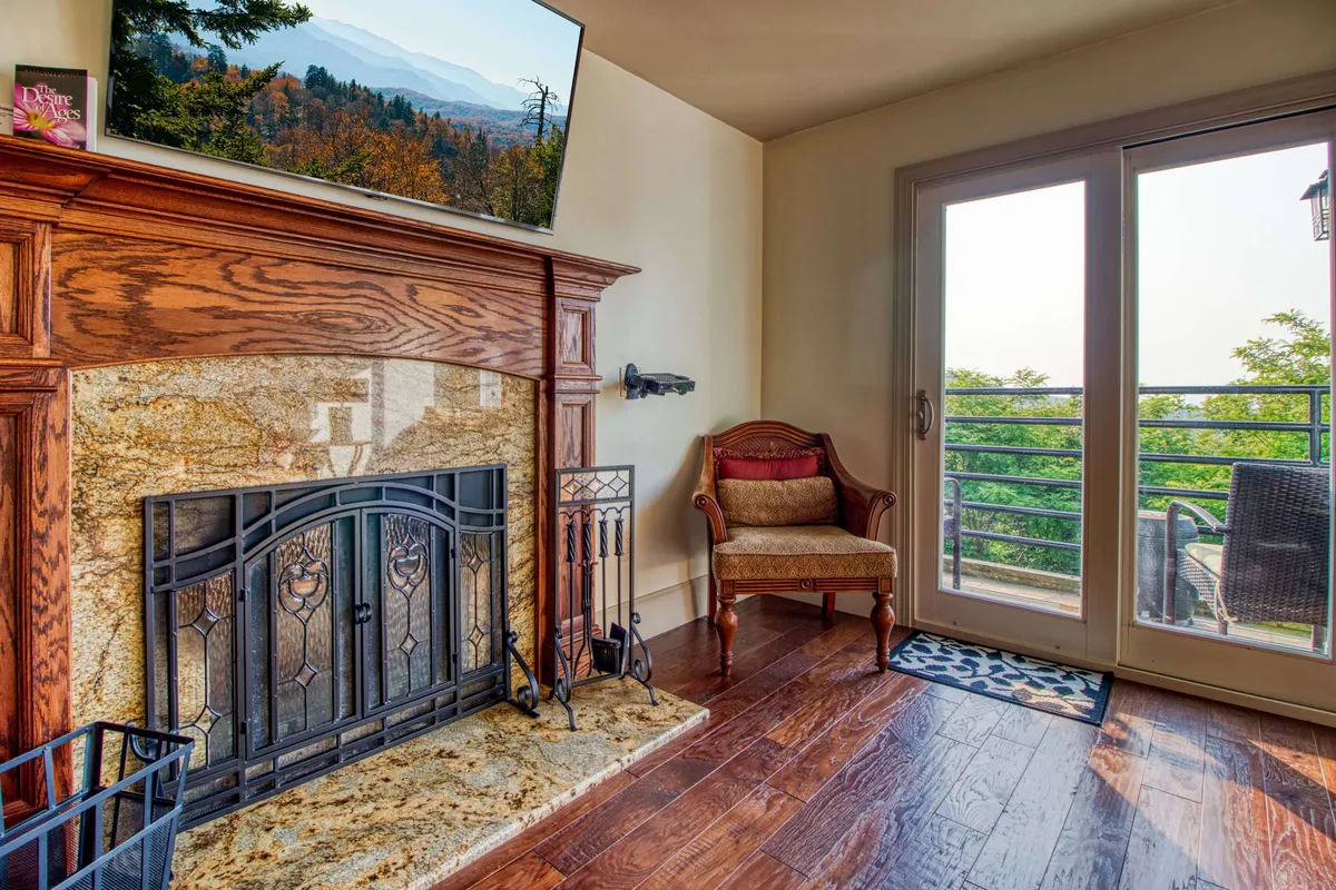 A comfortable and serene living room featuring a fireplace, armchair, and expansive glass doors that open to breathtaking mountain vistas. The room is bathed in natural light, emphasizing the inviting atmosphere and connection to the outdoors.