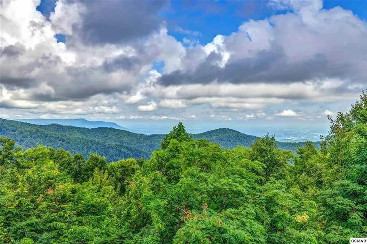 This image captures rolling mountains blanketed in dense green foliage beneath a dramatic sky. The peaceful atmosphere suggests early morning or late evening light, inviting viewers to imagine the fresh air and tranquility of the Great Smoky Mountains. The scene hints at the vast opportunities for hiking, birdwatching, and relaxing in nature.