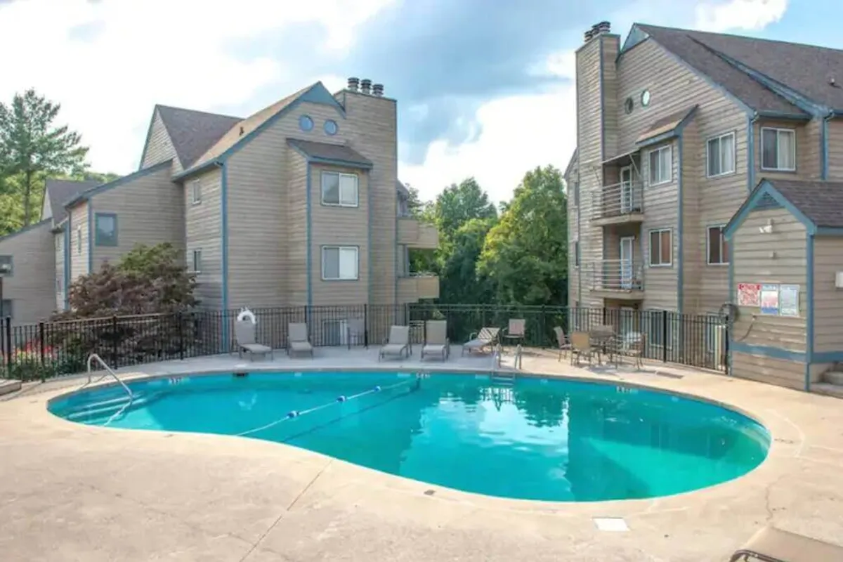 A sparkling swimming pool surrounded by lush greenery and condo buildings, with lounge chairs set up for socializing and relaxing. The pool is a focal point for families, offering both activity and relaxation after a day of exploring.