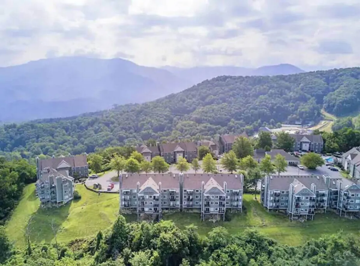 This exterior image showcases a serene mountain range in the distance, with apartment buildings nestled among lush greenery. The scene suggests the inviting natural setting surrounding the property and hints at outdoor activities like hiking and sunset watching.