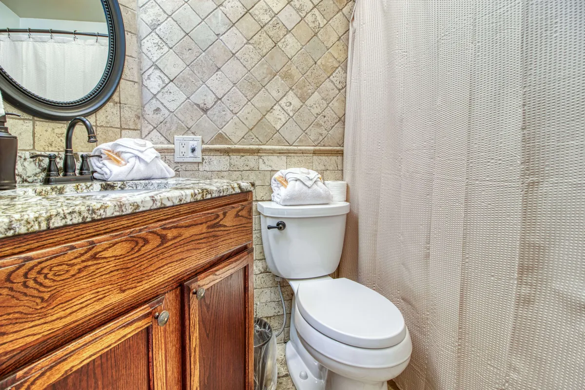 A clean and inviting bathroom featuring a granite countertop, a large mirror reflecting soft lighting, and neatly arranged towels. The ambiance suggests a fresh, peaceful space for morning routines or relaxing baths.