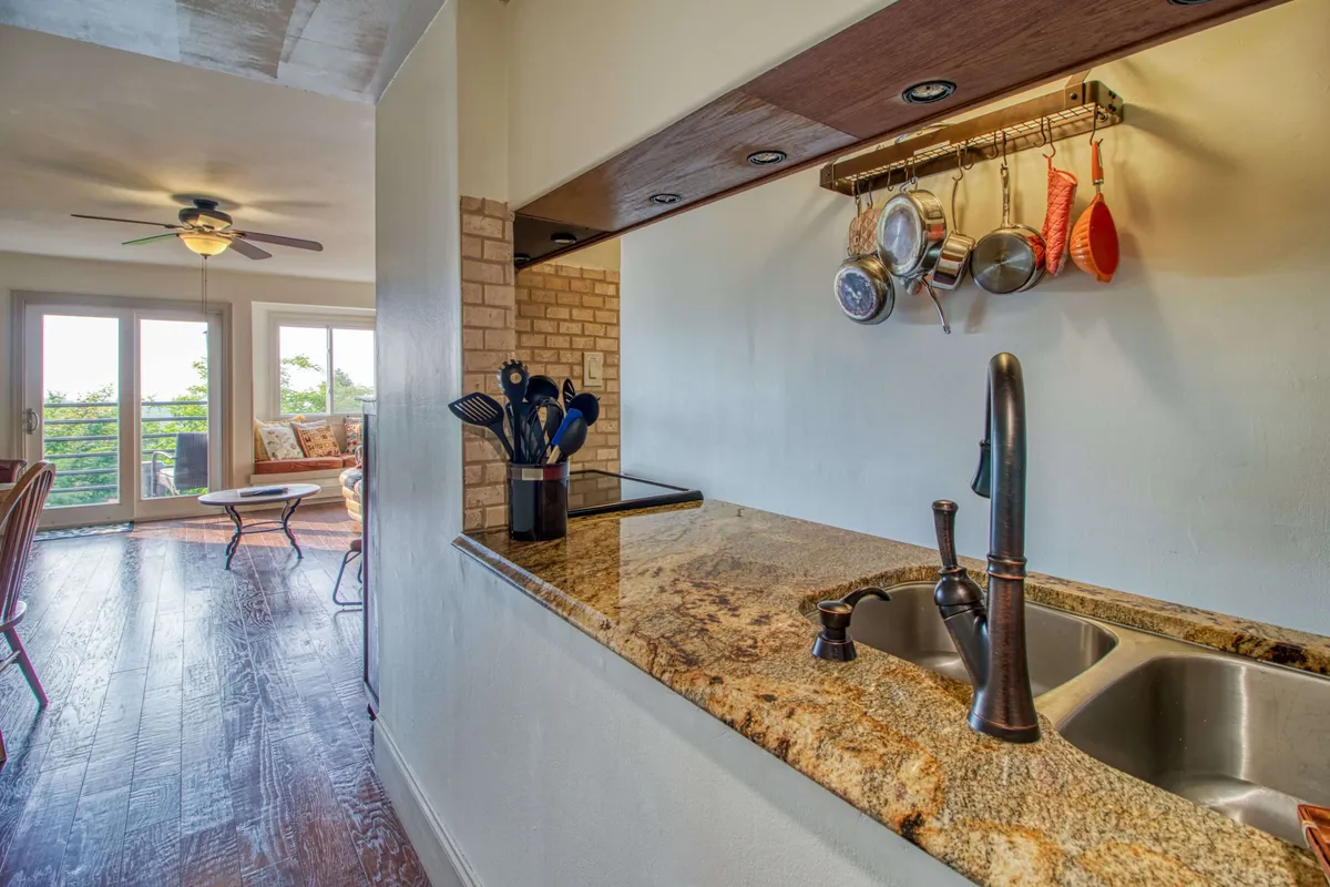 A welcoming kitchen scene with a prominent granite countertop, kitchen utensils displayed neatly, and an open layout that suggests connection to adjacent living and dining areas. The setting feels inviting and functional, ideal for both cooking and entertaining.