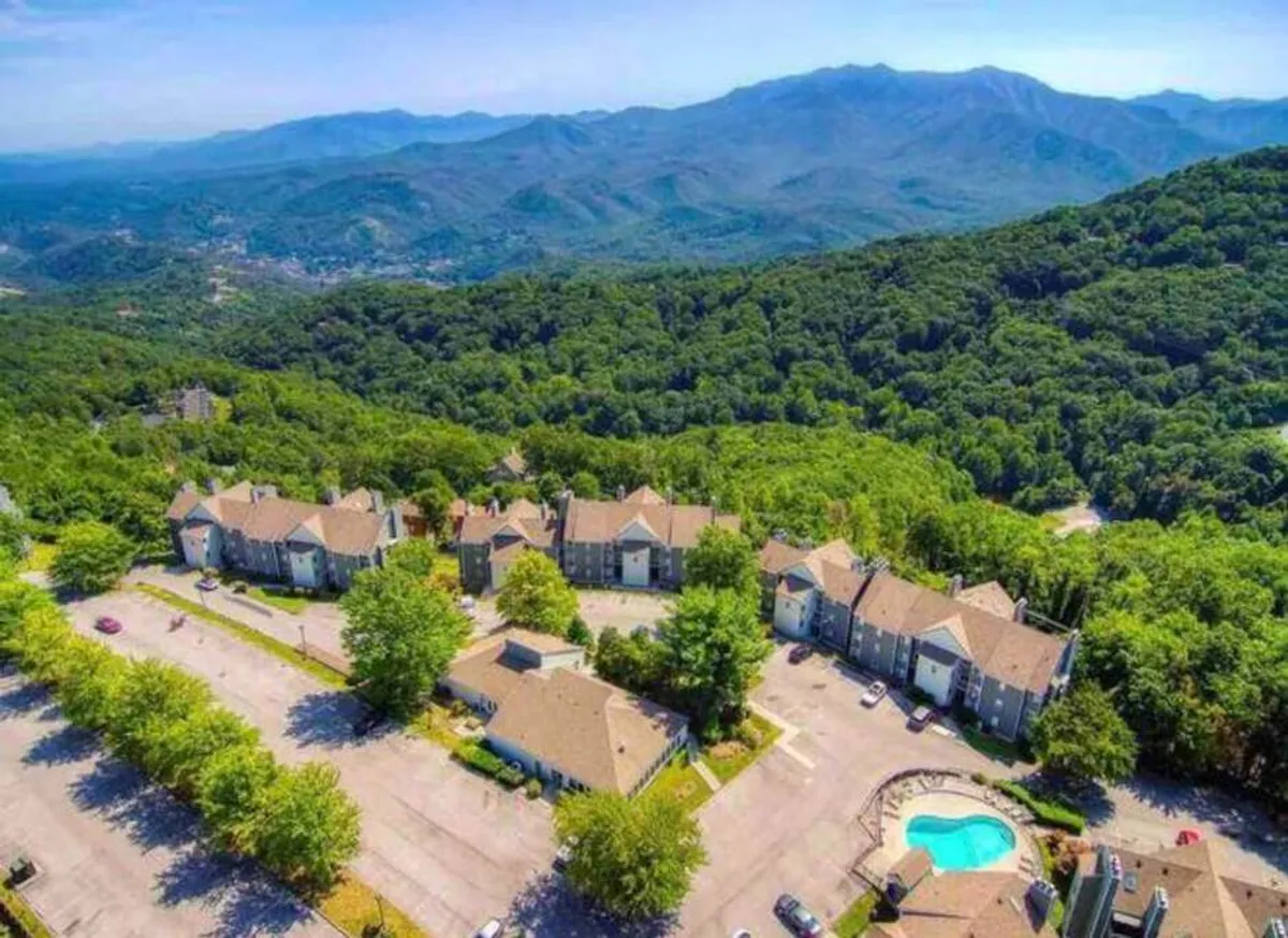 An exterior shot featuring a sparkling swimming pool framed by mountain ranges, townhouses, and lush trees. The area looks peaceful, hinting at opportunities for late-night swims under the stars or relaxing outdoors after a day of adventure.