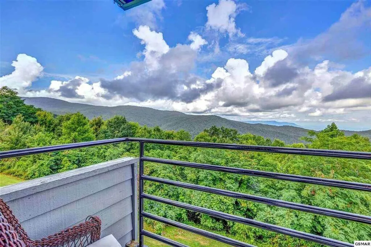 A stunning balcony view opens up to a sweeping panorama of the Smoky Mountains, with rolling green hills and a vast, colorful sky. The balcony's railing frames the landscape, inviting guests to relax, sip their morning coffee, or savor a breathtaking sunset. The scene exudes tranquility and the promise of unforgettable moments immersed in nature.