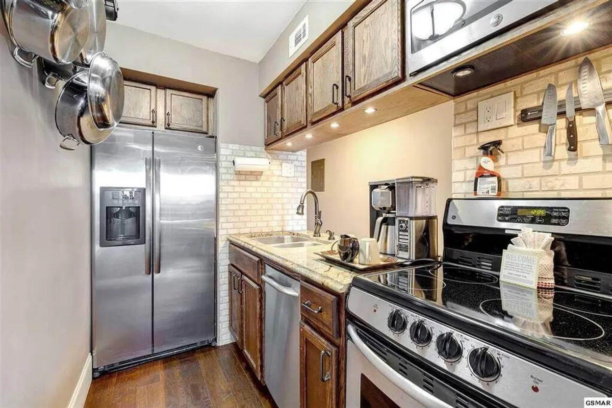 A bright kitchen interior with stainless steel refrigerator, granite countertops, wooden cabinets, and contemporary kitchen appliances. The arrangement creates a sense of openness and warmth, perfect for family gatherings or entertaining guests.
